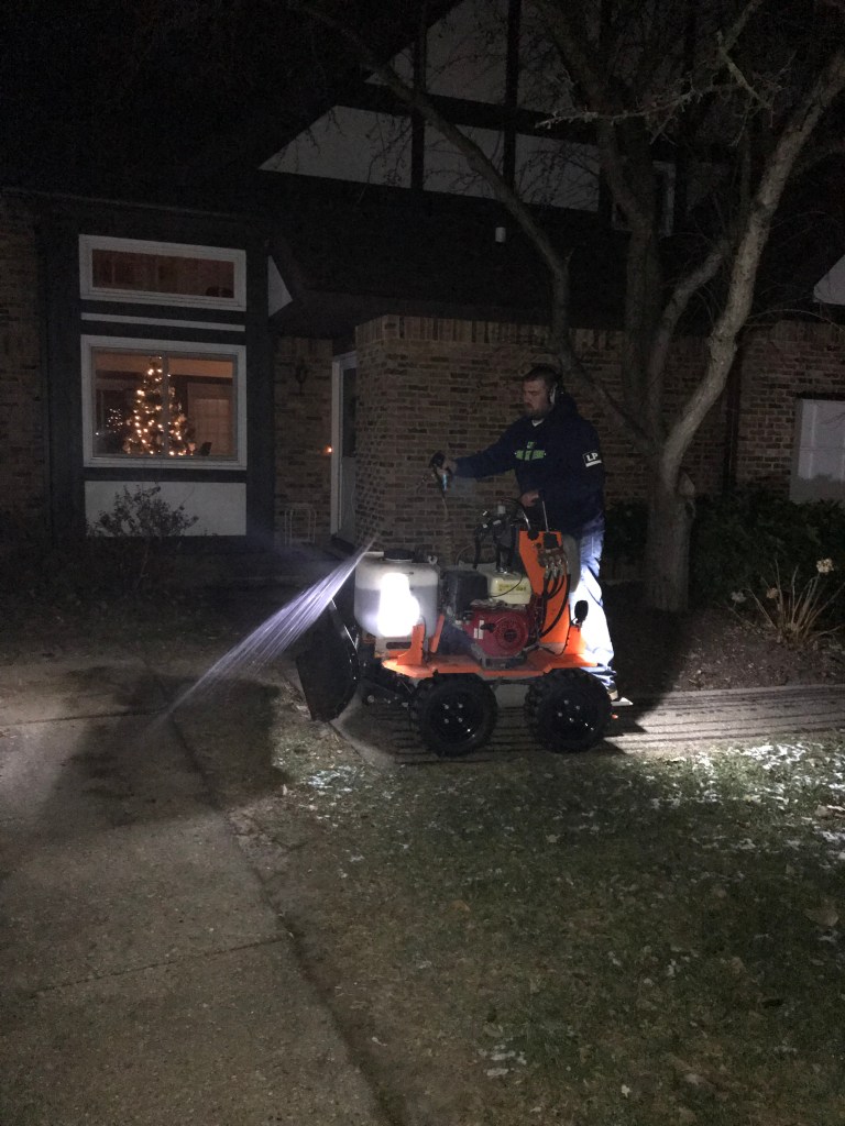 Man on tractor spraying a stream of liquid onto sidewalk